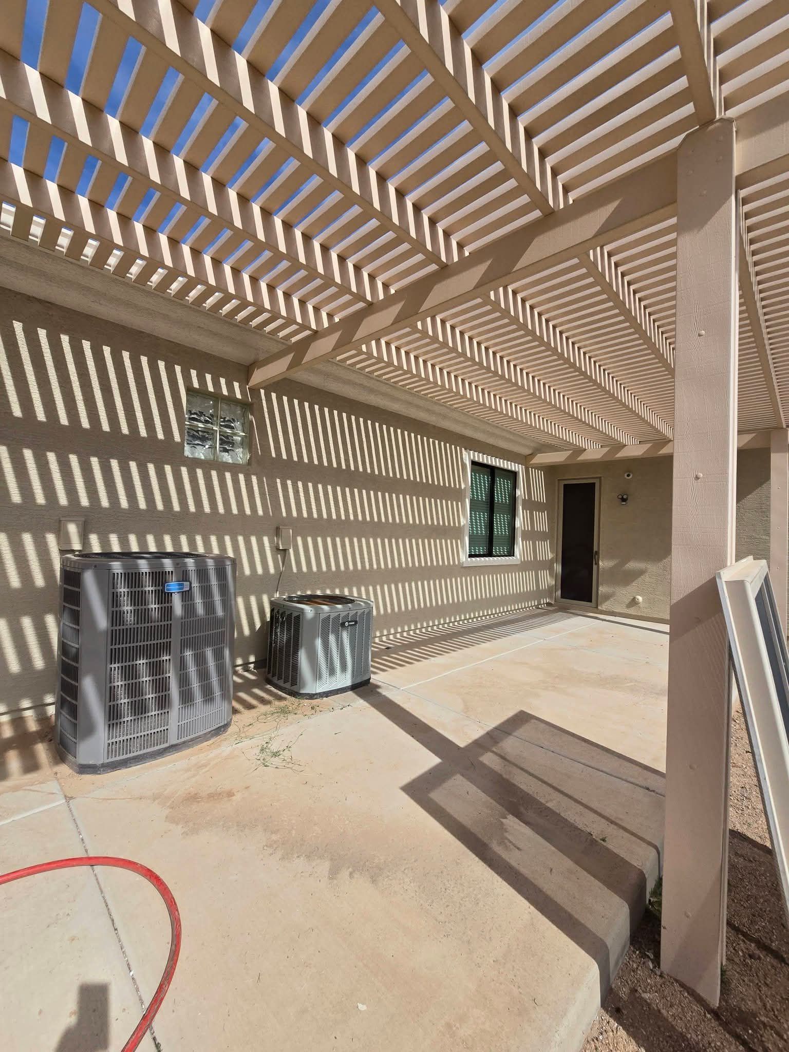 Covered patio with slatted pergola casting striped shadows on beige walls and concrete floor.