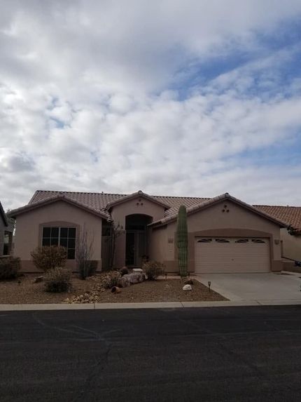 Single-story beige stucco house with a two-car garage and desert landscaping under a cloudy sky