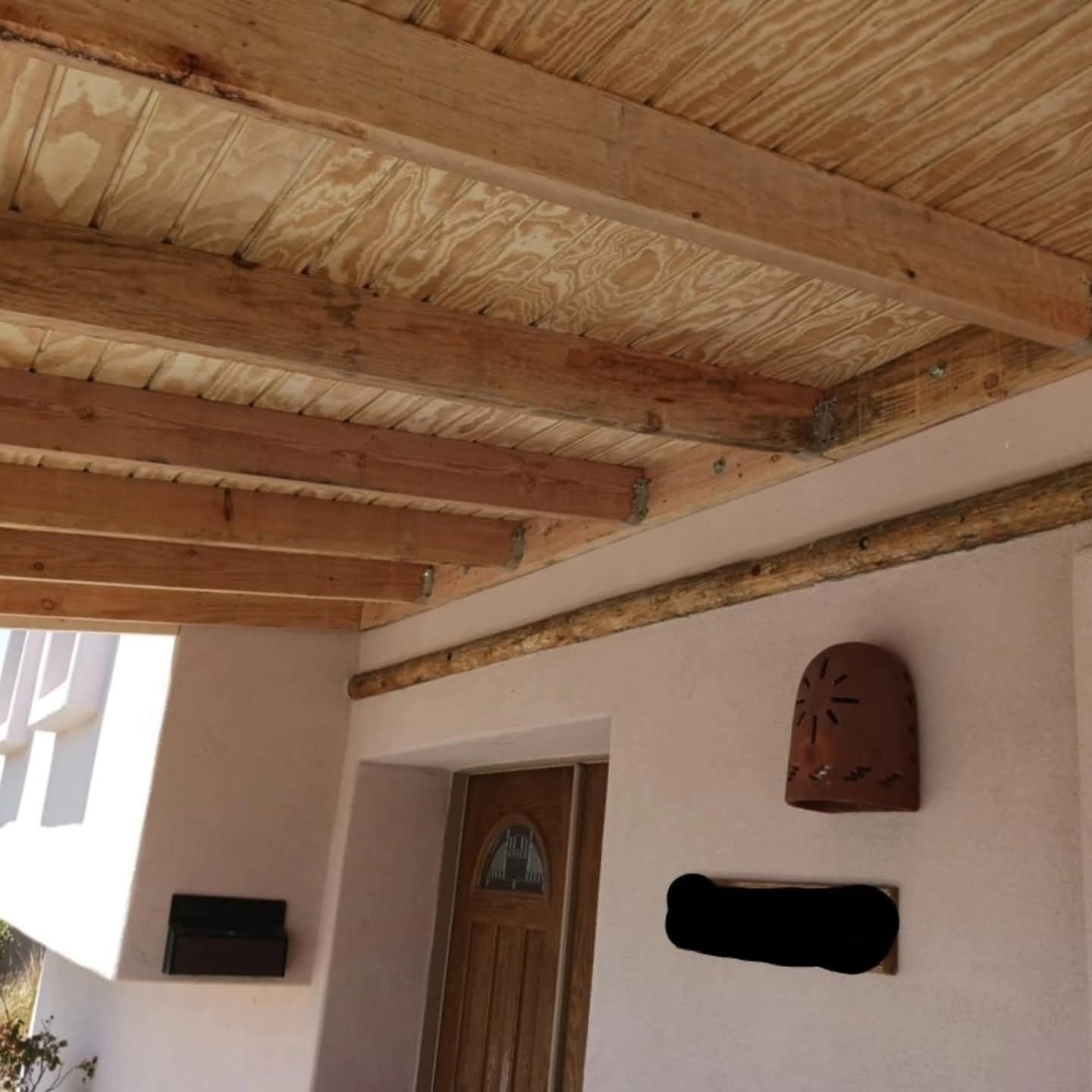 Covered patio ceiling with wooden beams, a wooden door, and wall-mounted decor on a stucco wall