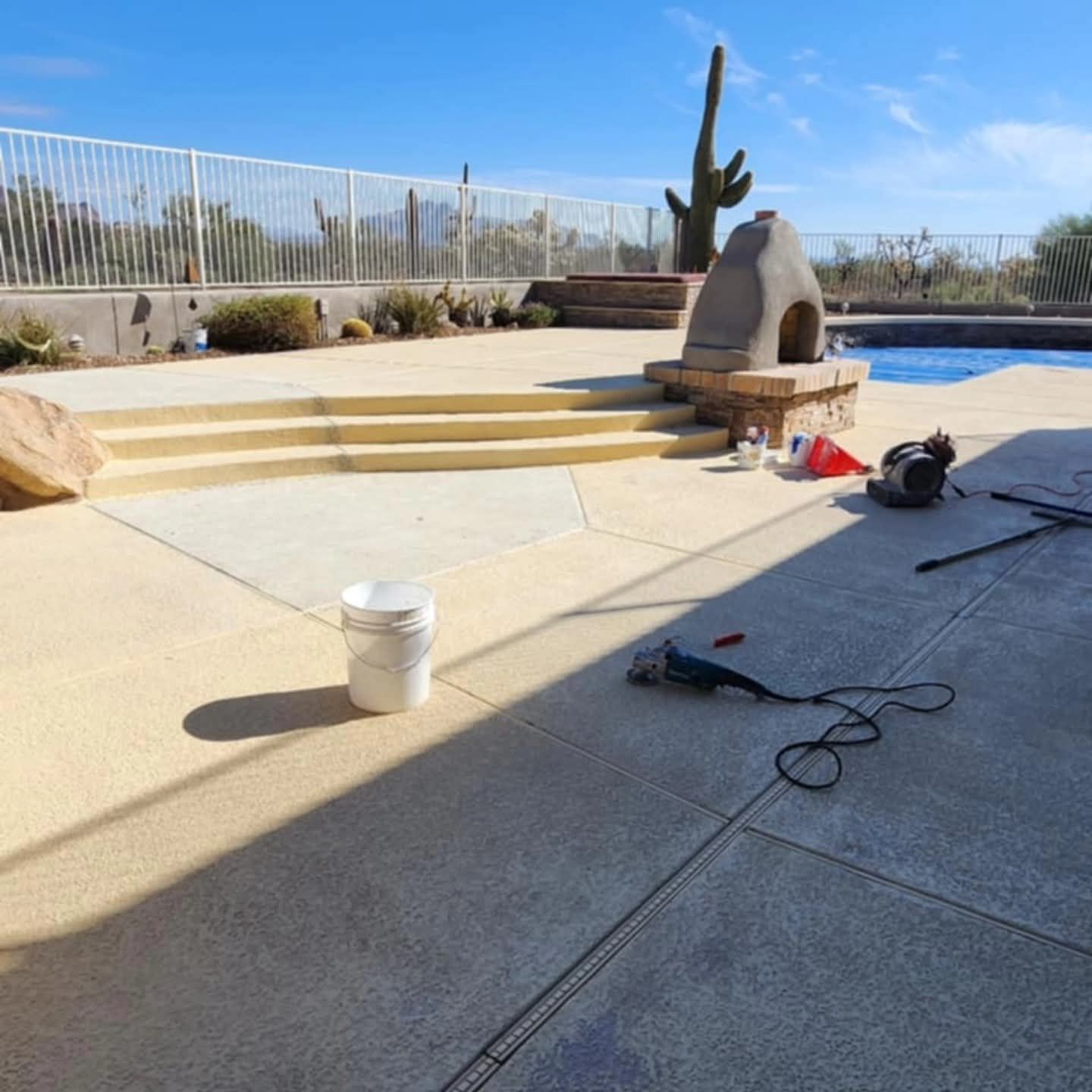 Backyard pool deck with steps, cactus decor, bucket, and power tools on the ground