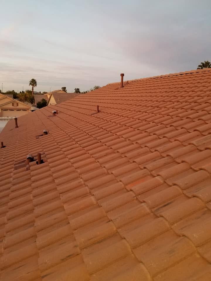 Terracotta-tiled rooftops under a pastel evening sky, with distant palms and chimneys
