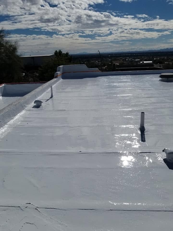 White rooftop with reflective coating under a cloudy blue sky, viewed across a low horizon.