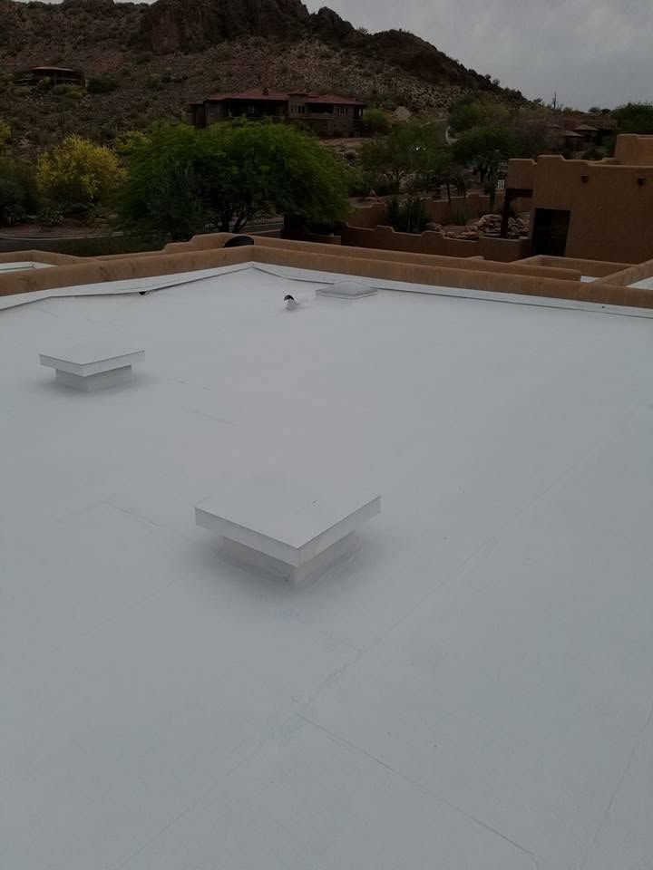 White flat rooftop with two small vents, surrounded by desert hills and adobe-style buildings.