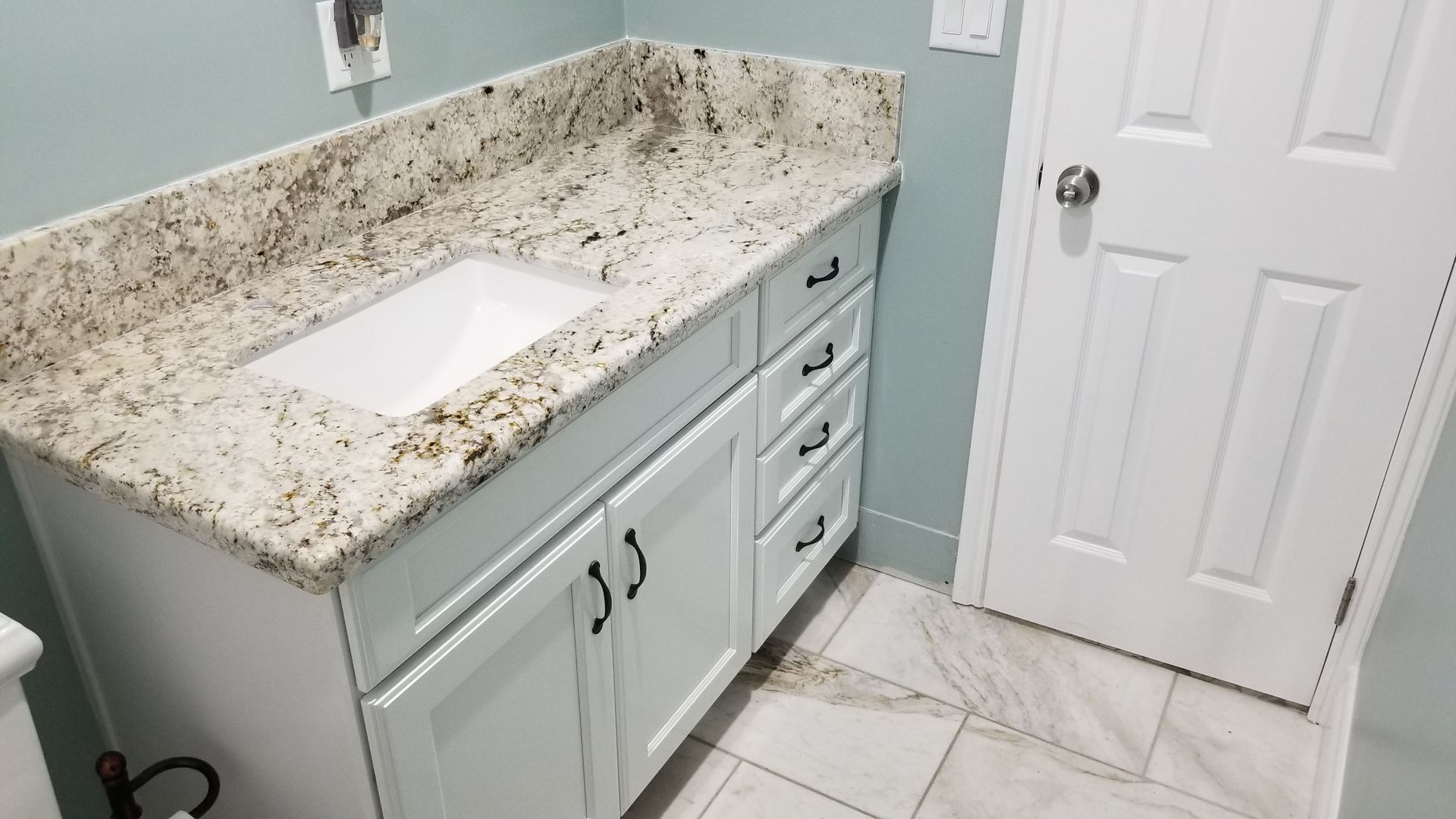 Bathroom vanity with white sink, speckled granite countertop, light blue cabinets, and tiled floor.