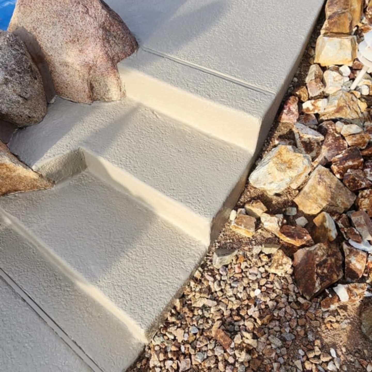 Concrete steps beside a rocky garden bed with light tan gravel and large stones