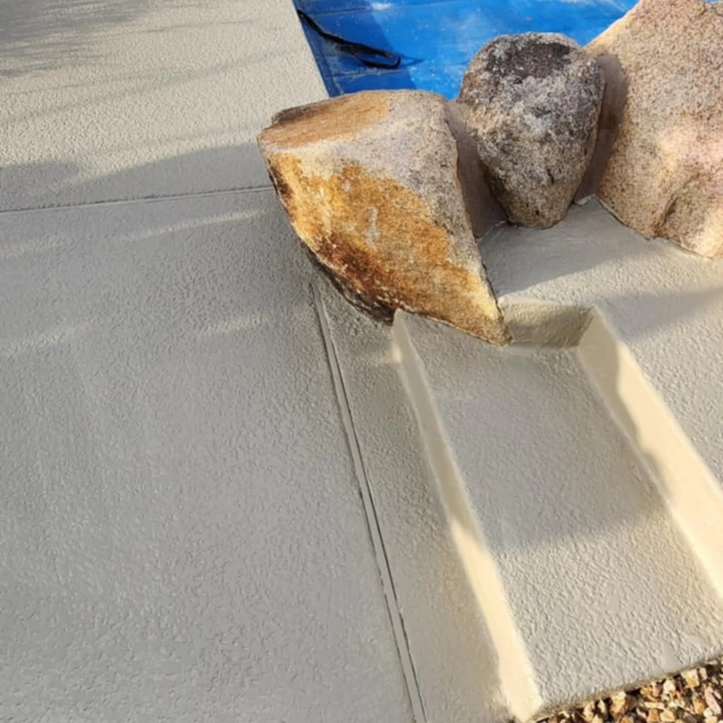 Close-up of tan stucco wall with large decorative rocks on top in sunlight