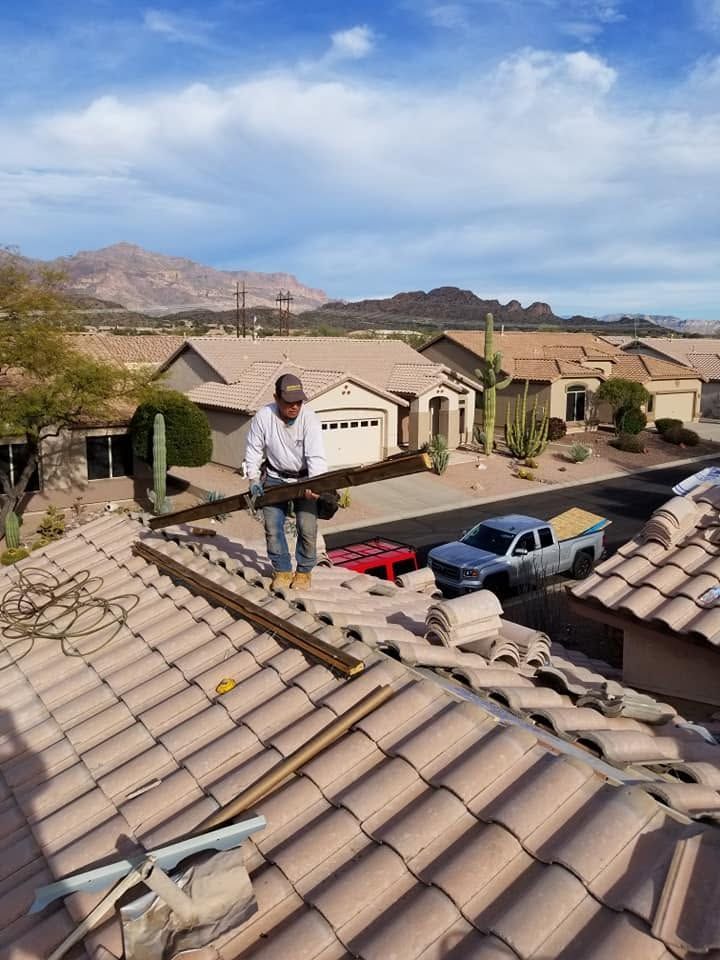Worker on a tiled suburban rooftop beside parked cars and desert hills.