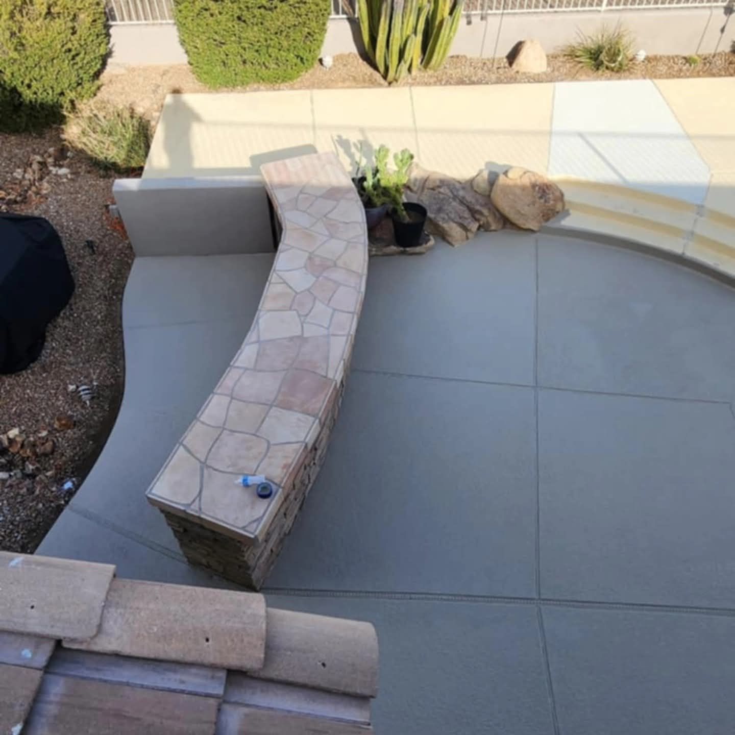 Curved stone bench on a tiled patio with potted plants and desert landscaping nearby