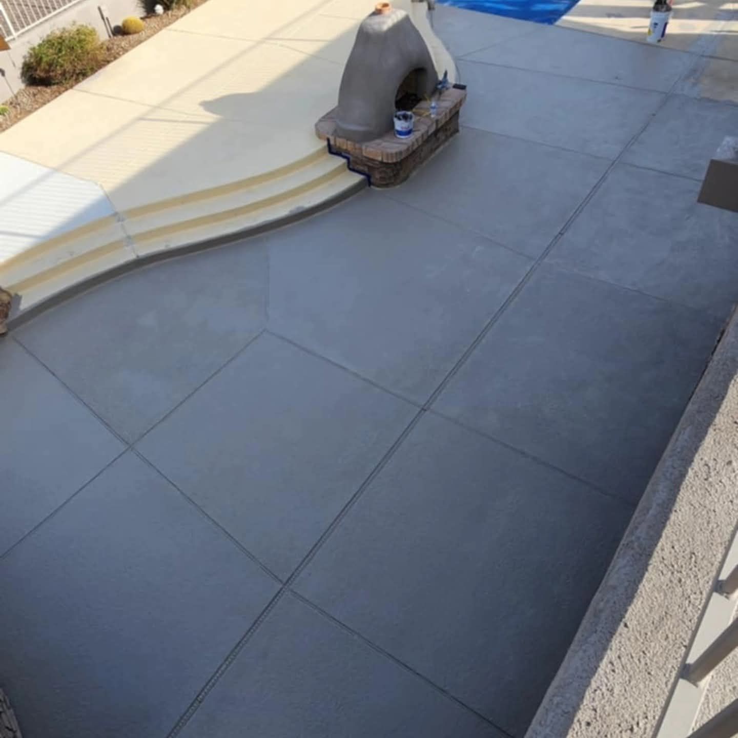 Empty gray concrete patio with curved steps, outdoor fireplace, and blue pool cover in the corner