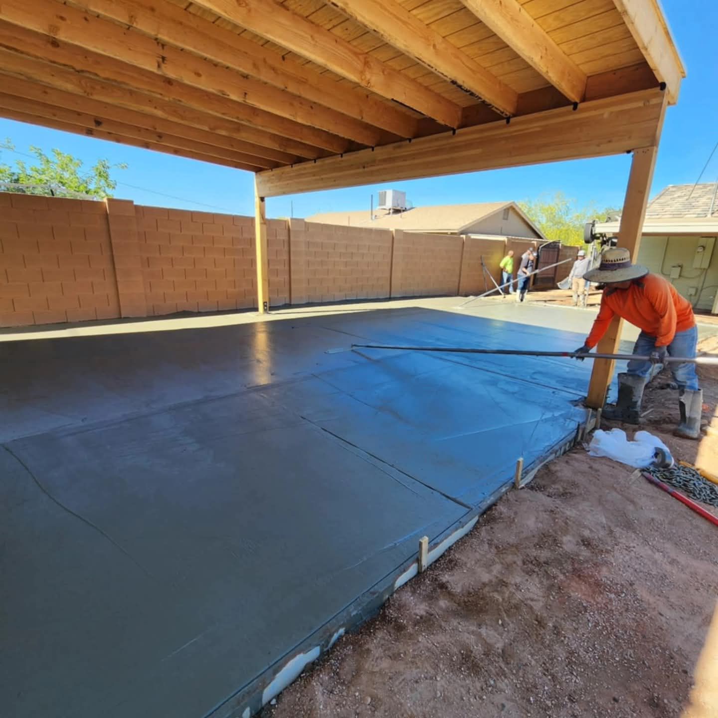 Worker smoothing fresh black concrete under a covered patio in a fenced backyard