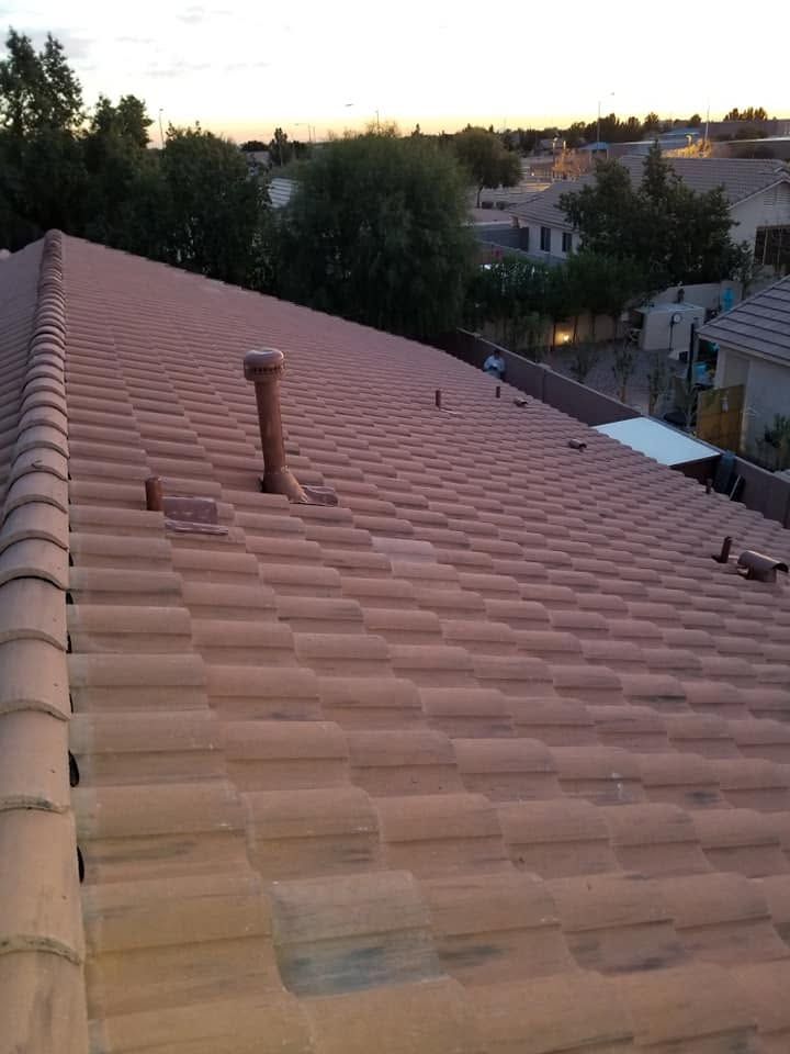 Rooftop with terracotta tiles and a vent pipe, overlooking trees and houses at sunset