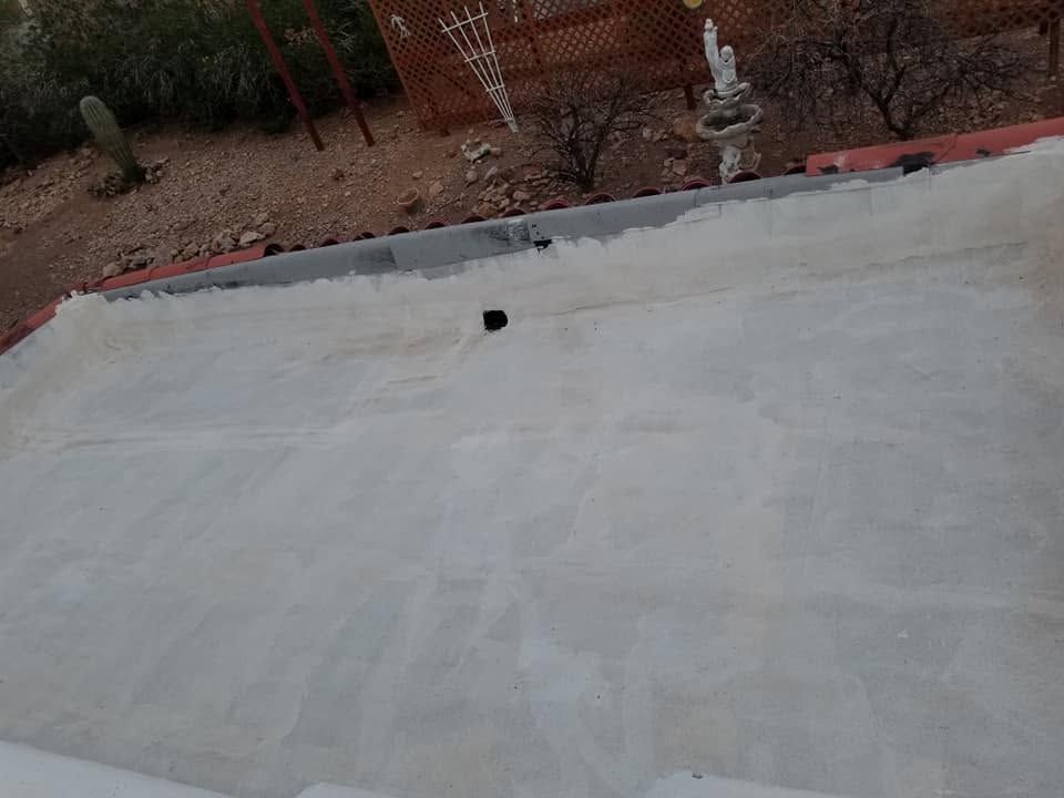 Flat white rooftop with a small black vent, bordered by brown rocks and shrubs.