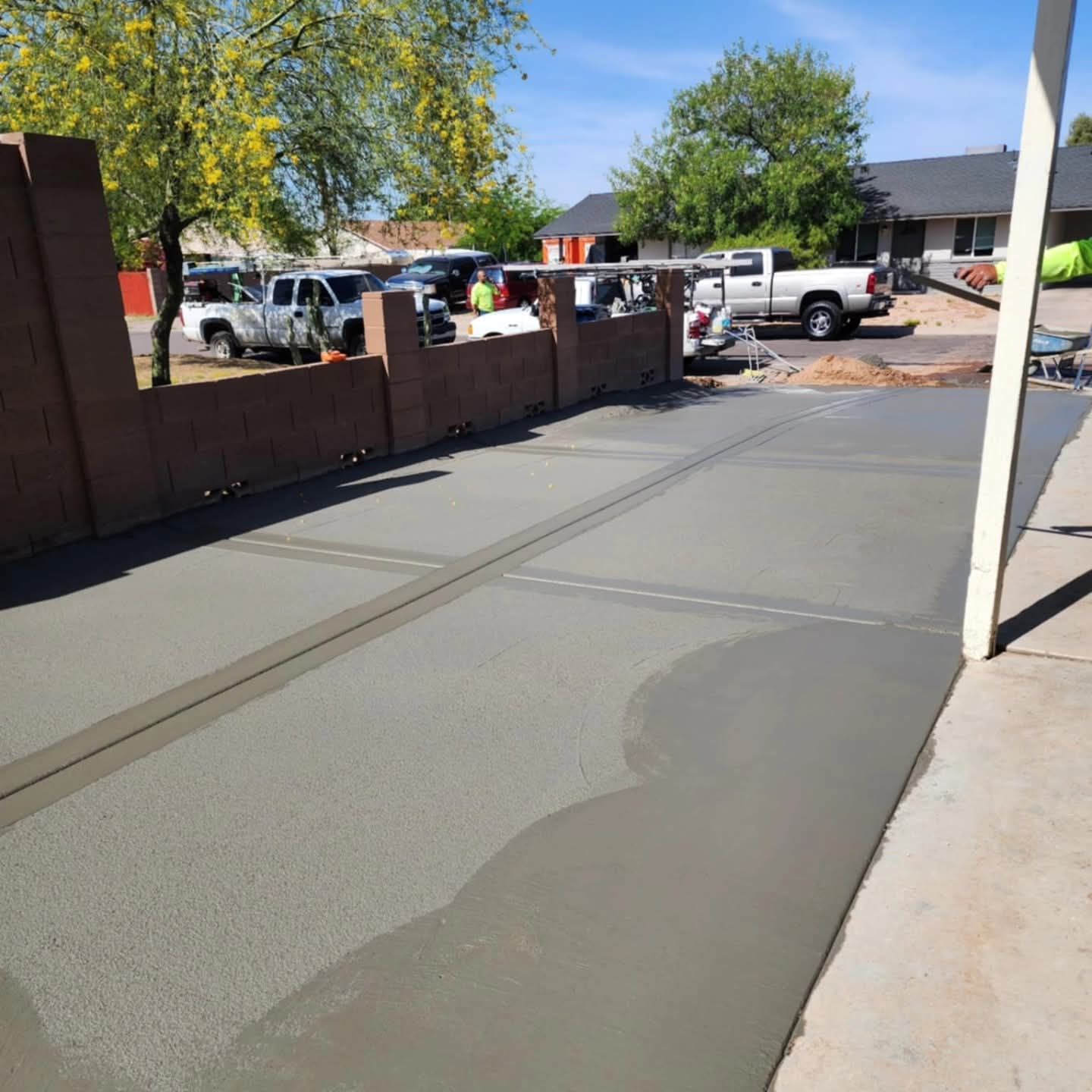 Freshly poured gray concrete sidewalk beside a residential street with parked trucks and trees in the background