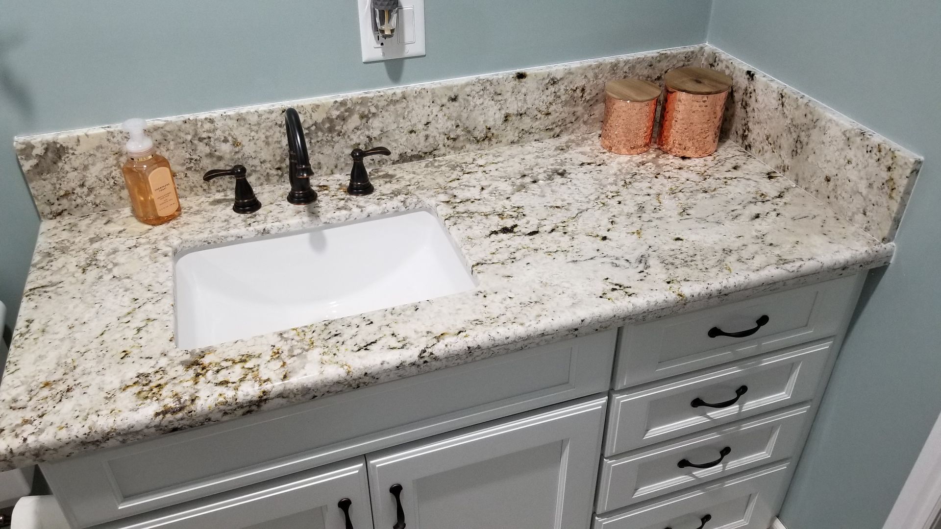 Bathroom vanity with speckled granite countertop, white sink, and black faucet, with towels on the side.