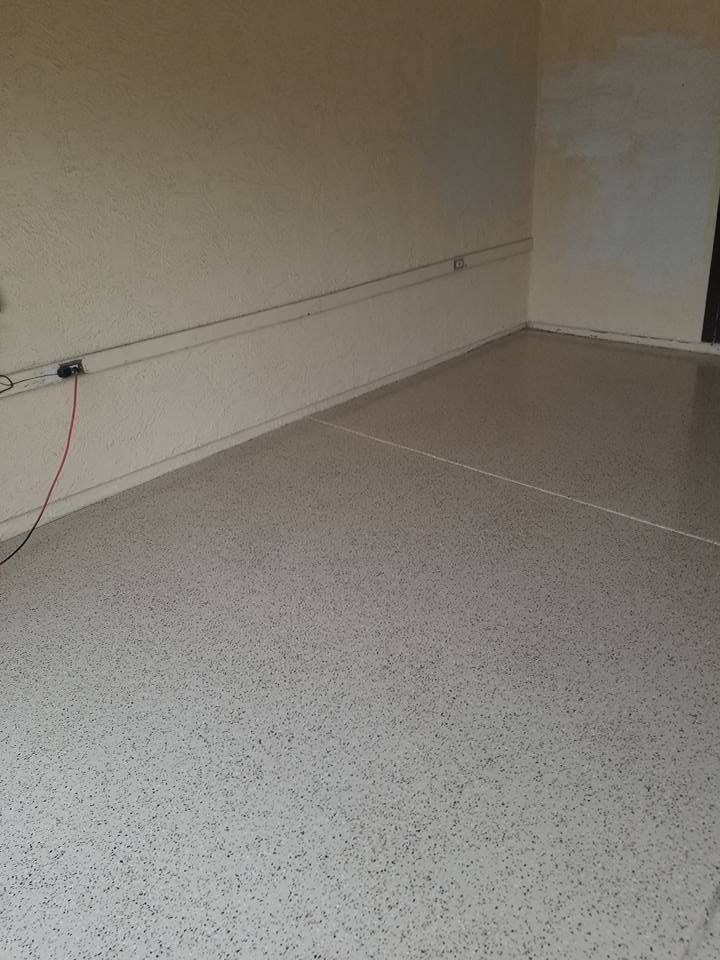 Empty speckled floor in a bare room with white walls and a power outlet along the baseboard