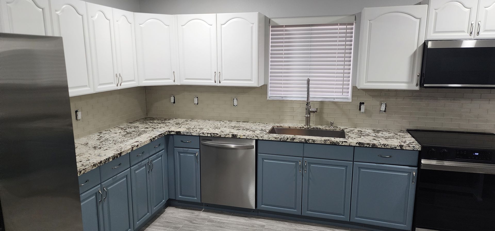 Modern kitchen with white upper cabinets, blue lower cabinets, granite counters, and stainless steel appliances