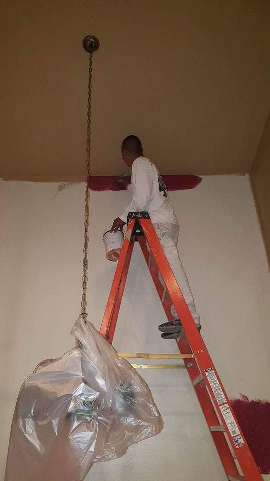 Person on an orange ladder reaching near the ceiling beside a hanging plastic-covered light fixture