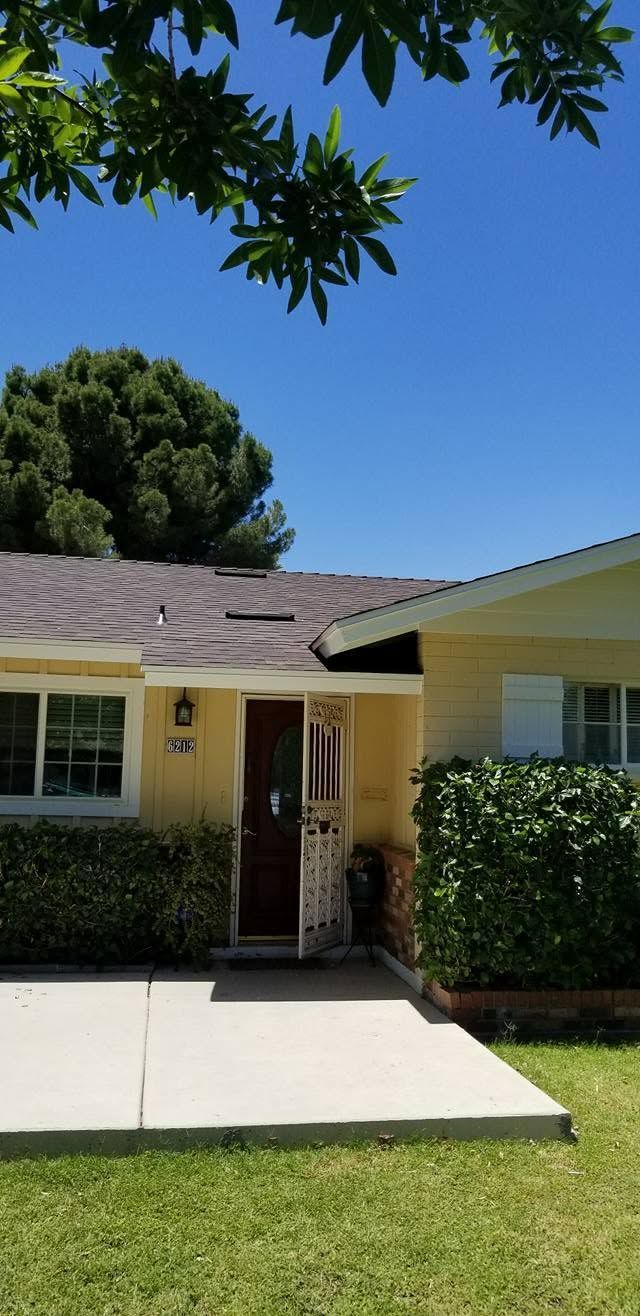 Single-story house with a front porch, hedges, and a concrete walkway under a clear blue sky