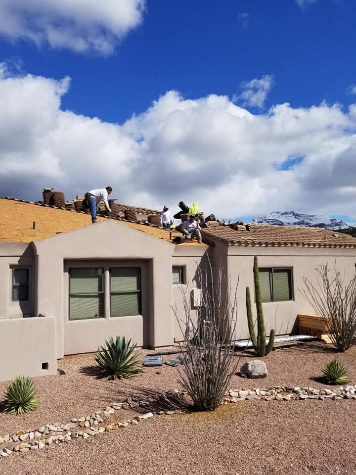 Roofers repairing a tan house roof under a bright blue sky, with desert landscaping below