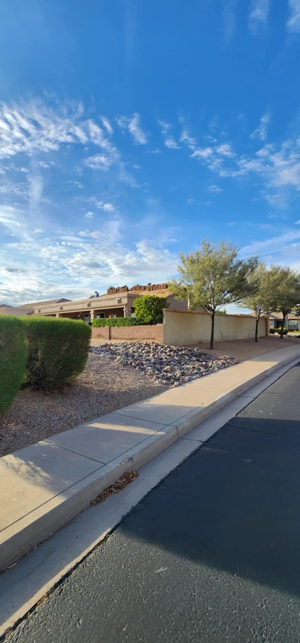 Sunny suburban street with sidewalk, desert landscaping, and a tan house under a blue sky