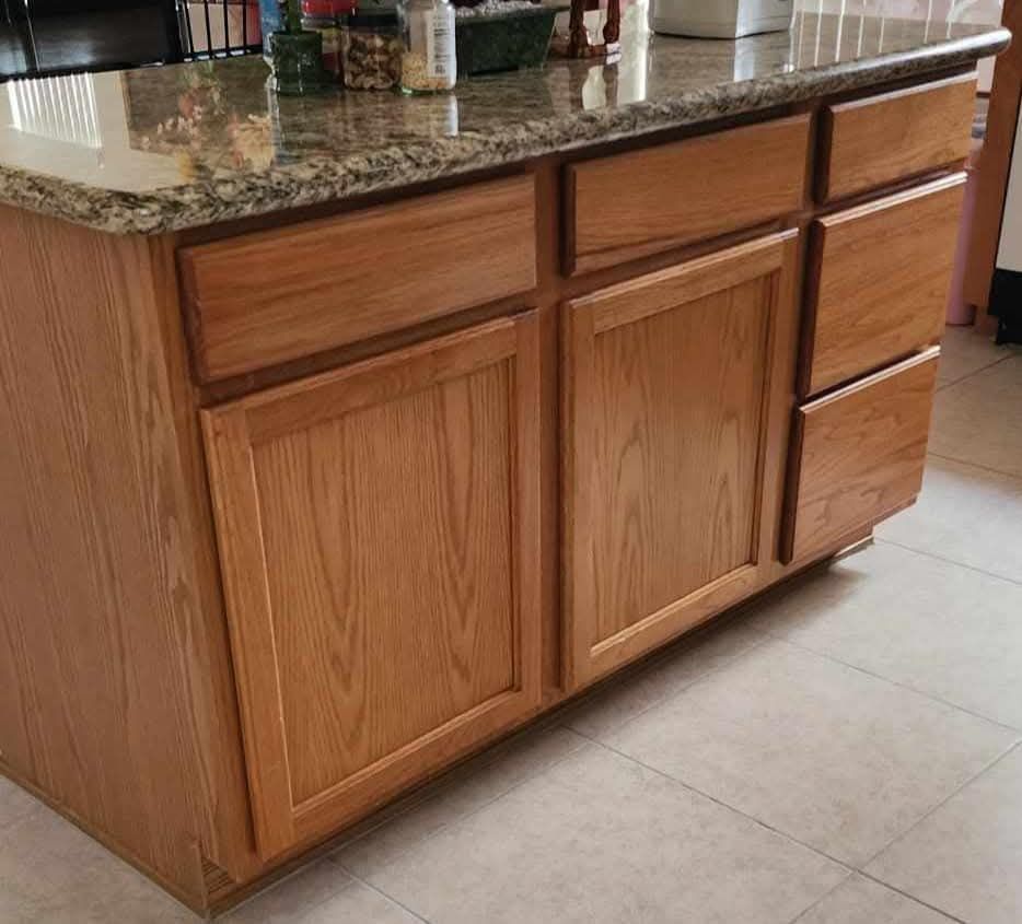 Wooden kitchen island with granite countertop and drawers on a tiled floor