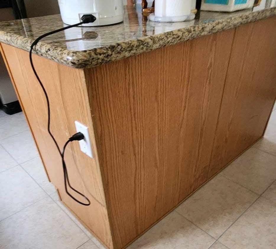Kitchen island with a granite countertop and a plugged-in cord hanging from the side panel