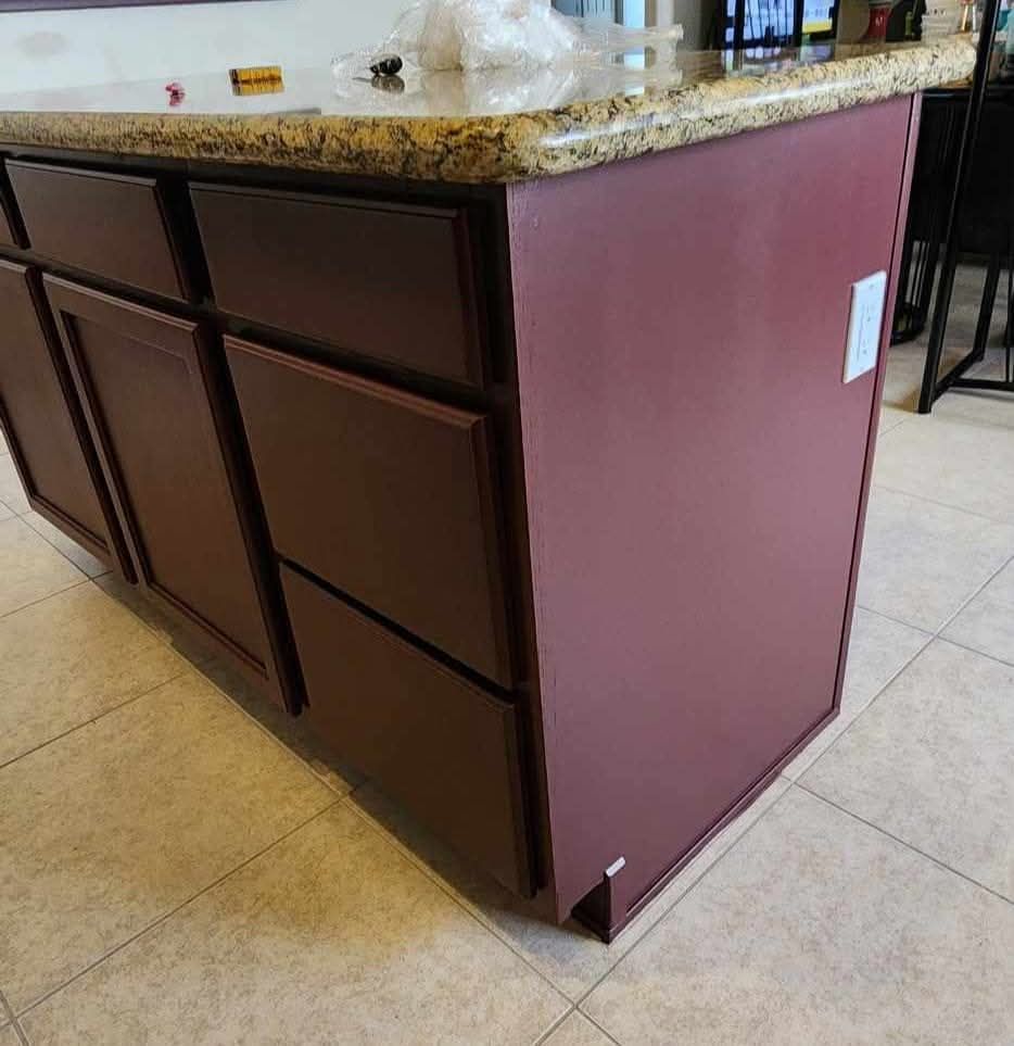 Kitchen island with dark paneled cabinets, maroon side, and granite countertop on tiled floor.
