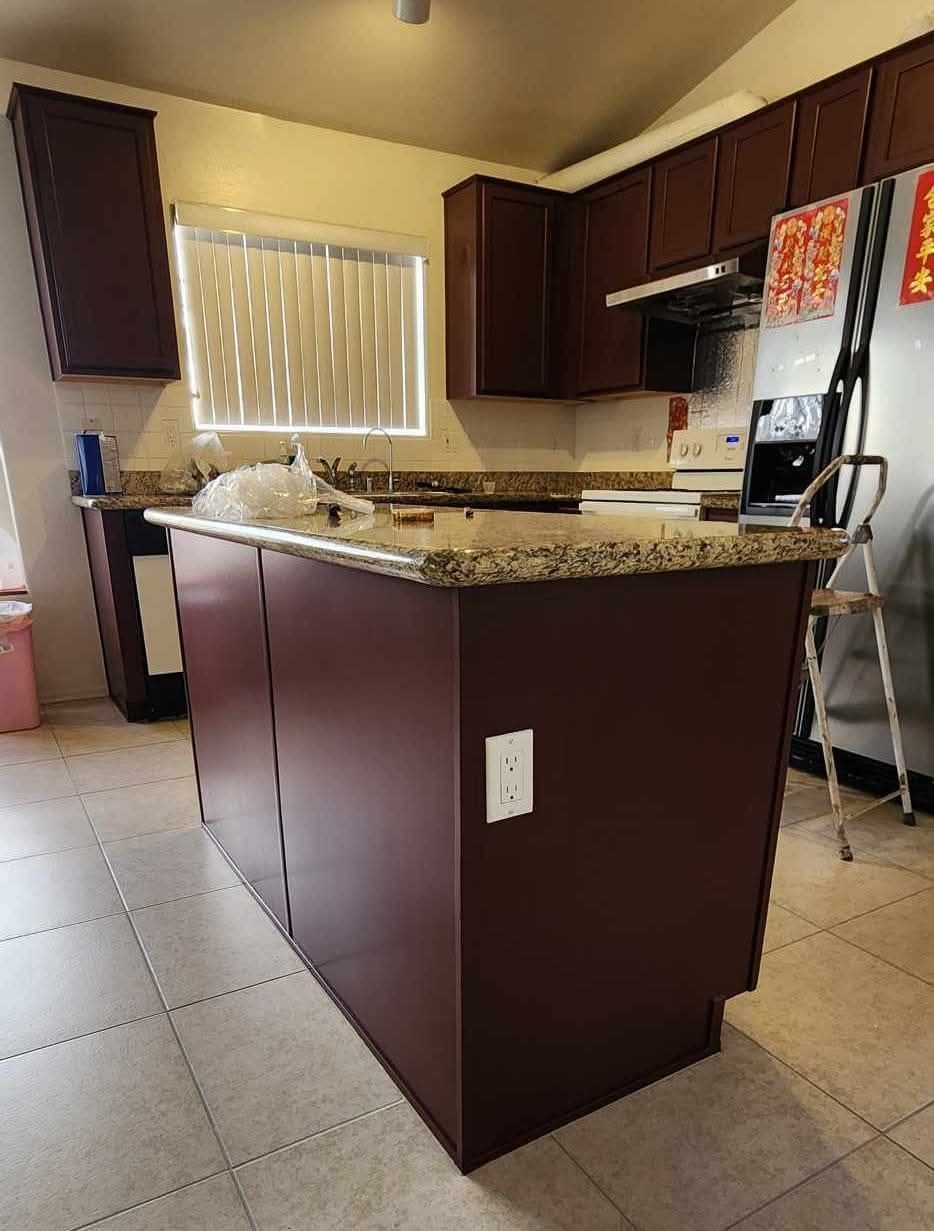 Kitchen with dark cabinets and granite island in a tiled room, with a sink and refrigerator.