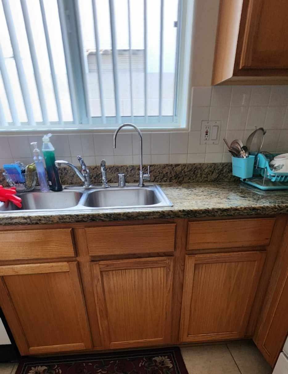 Kitchen sink and wooden cabinets beneath a window, with countertop items and a double basin sink.