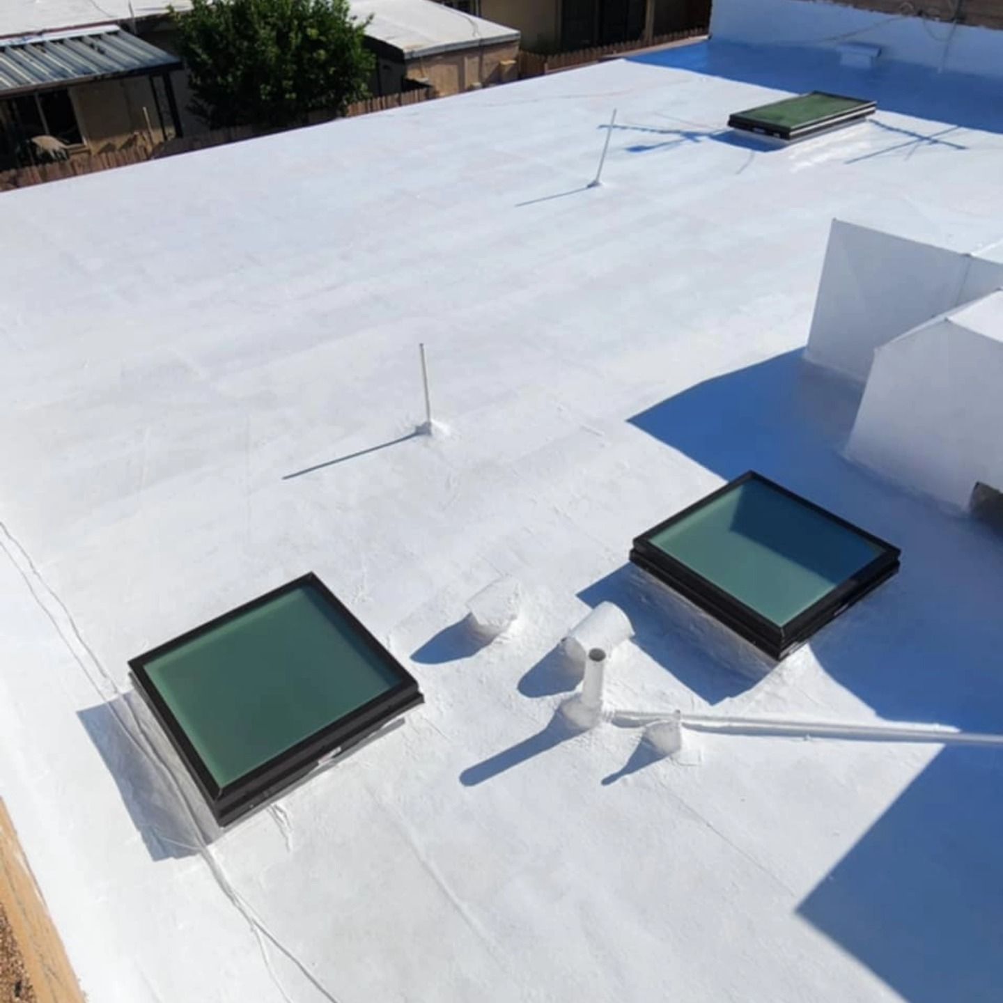 White flat rooftop with two square skylights and several vent pipes in bright sunlight
