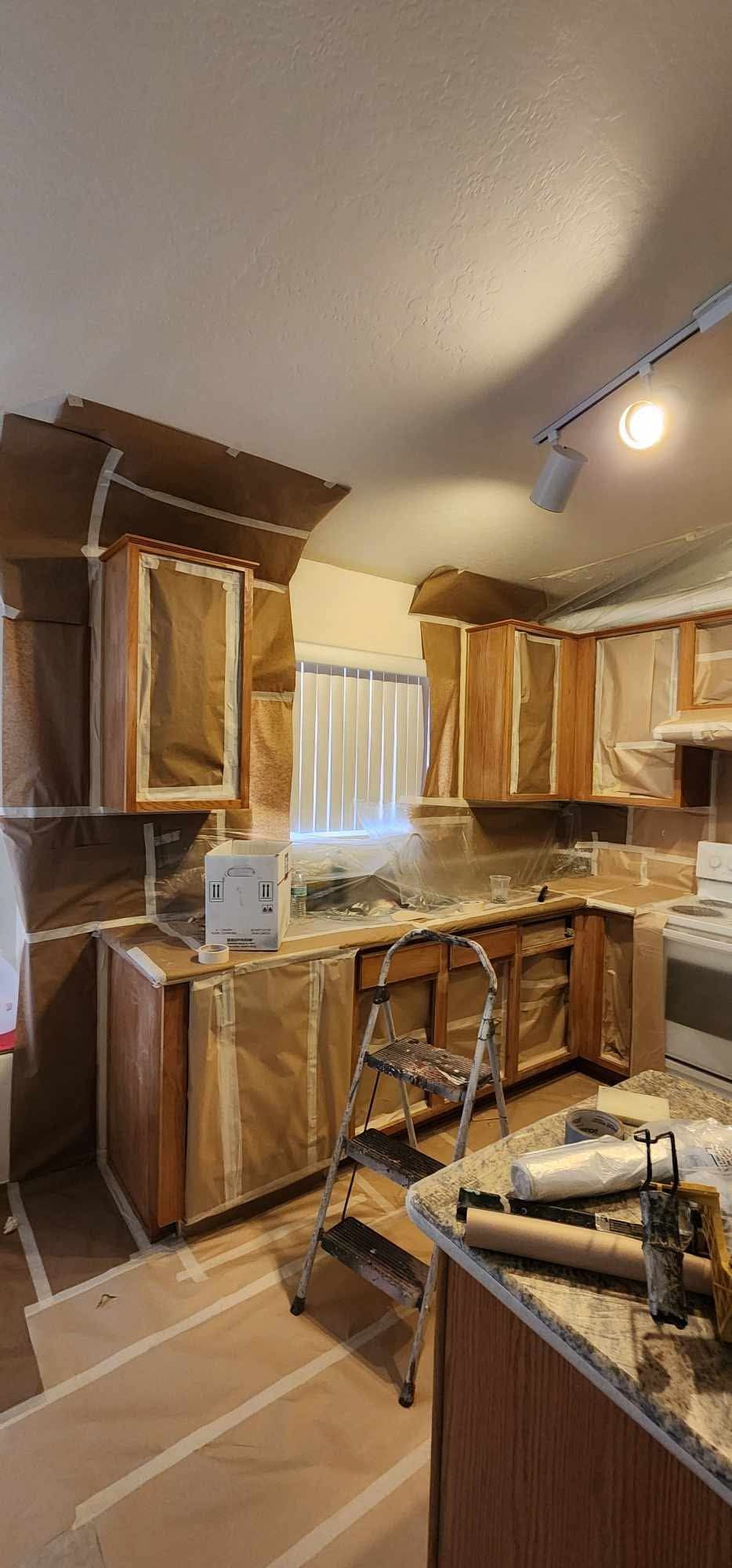 Renovating kitchen with taped cabinets, drop cloths, and tools scattered on the floor