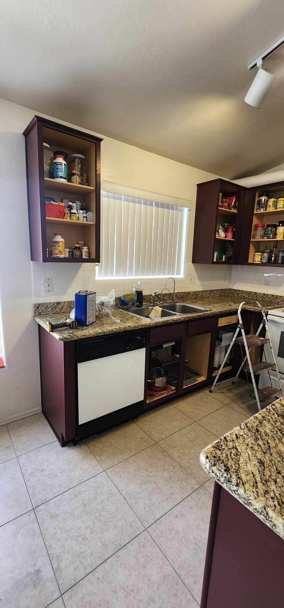 Small kitchen with granite counters, purple cabinets, white tile floor, and a window over the sink.