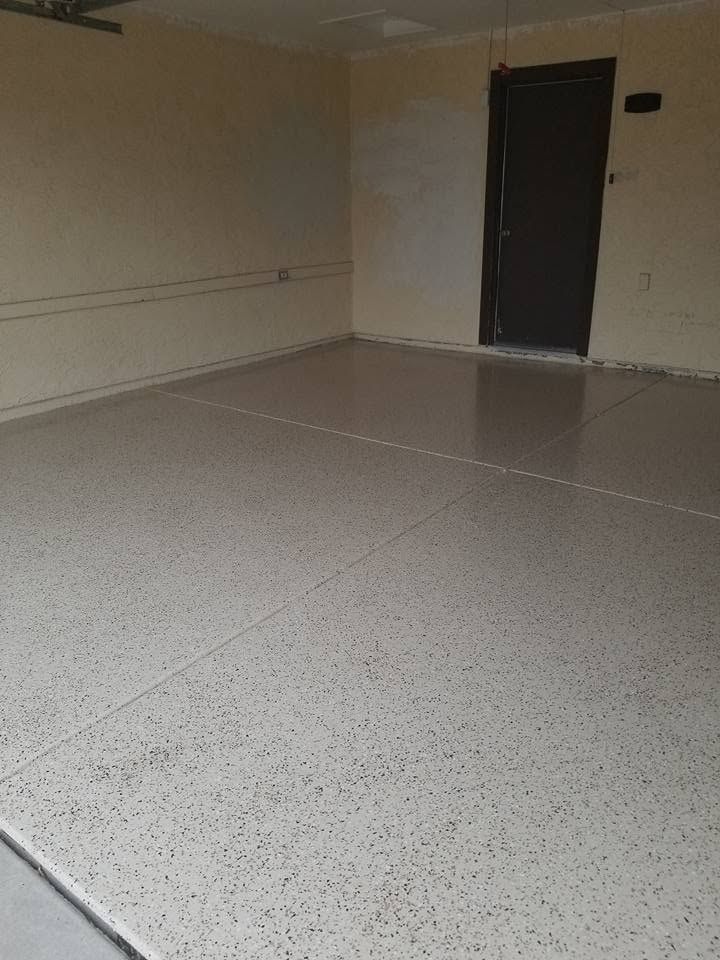 Empty room with speckled tile floor, beige walls, and a dark door at the back.