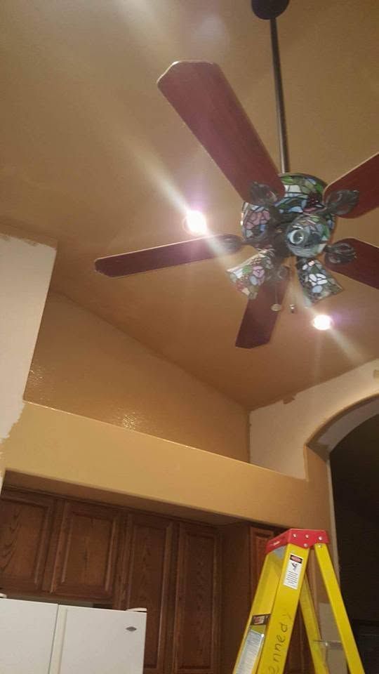 Ceiling fan with wooden blades and lights in a kitchen, with cabinets and a ladder below.
