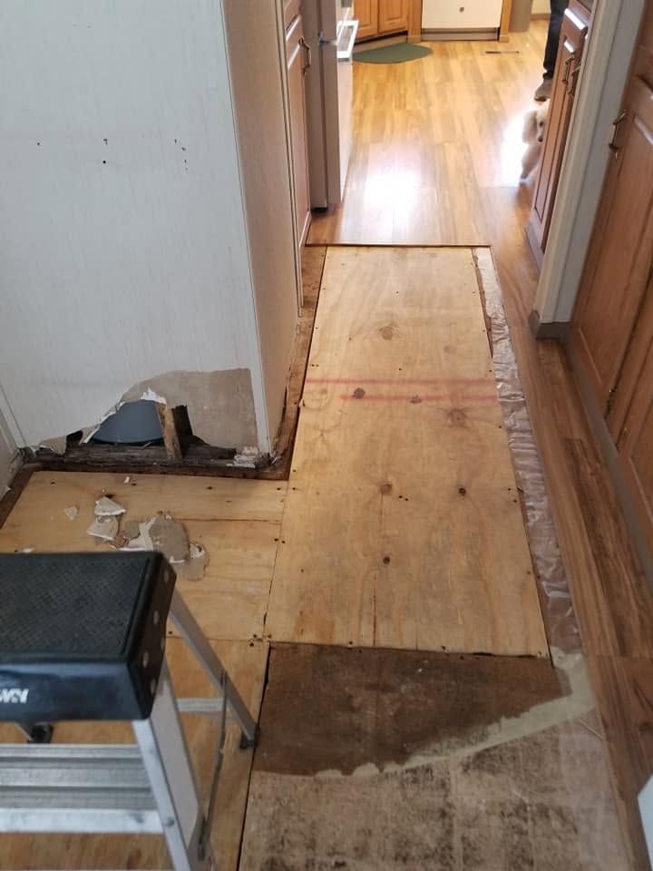Hallway with plywood floor patching and exposed repair area near a doorway