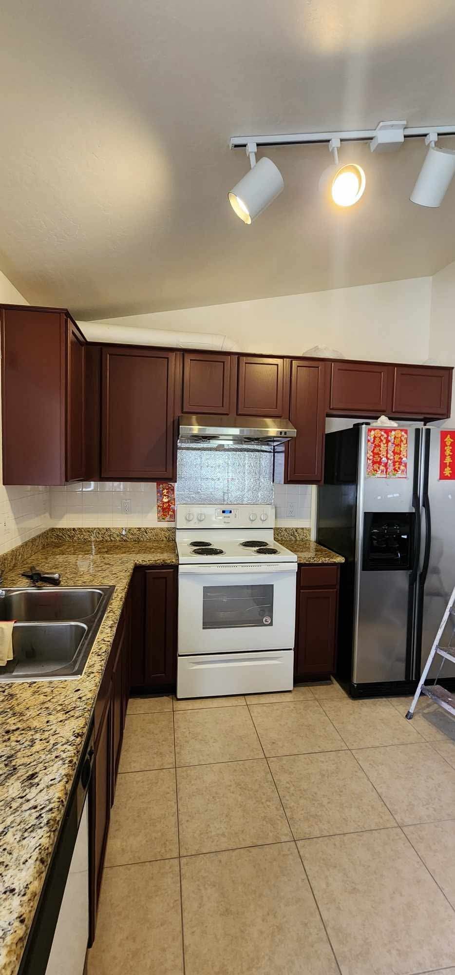 Small kitchen with white stove, dark cabinets, granite counters, and a black refrigerator under track lights