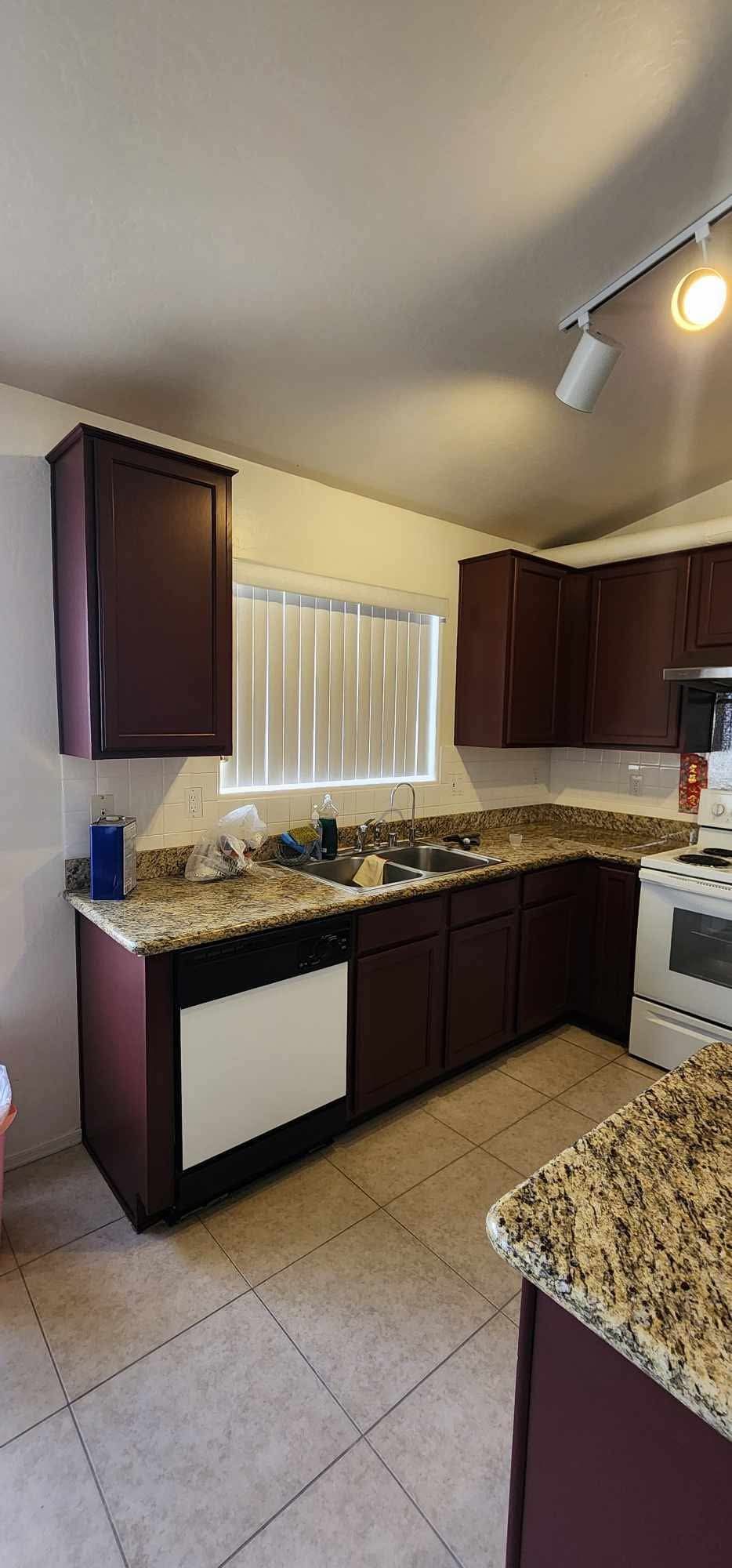Small kitchen with dark cabinets, granite countertops, tile floor, and a window above the sink.