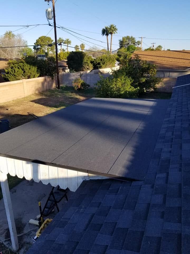 Flat gray roof with white awning beside a backyard, trees, and a utility pole under clear sky