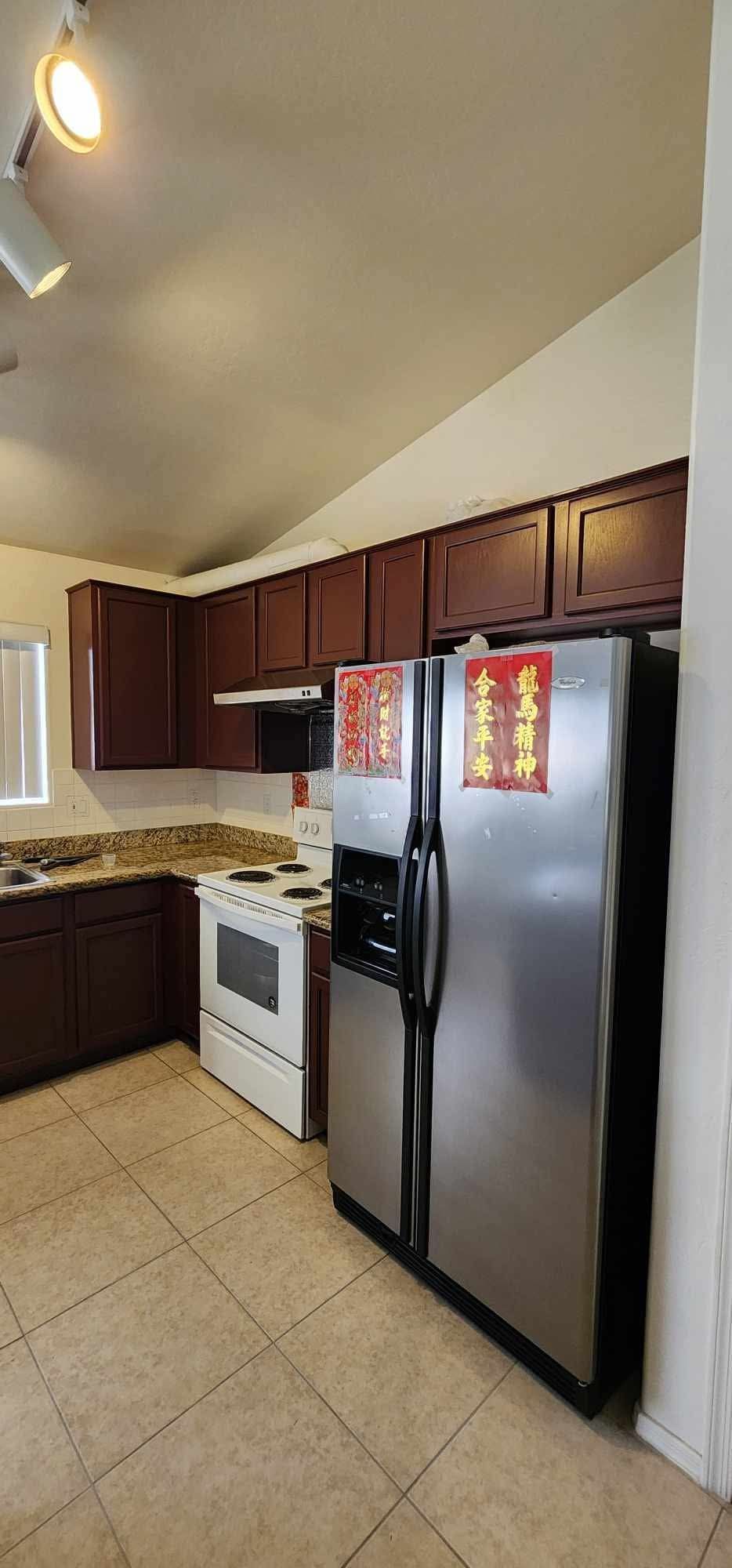 Small kitchen with dark wood cabinets, stainless fridge, white stove, and beige tile floor.