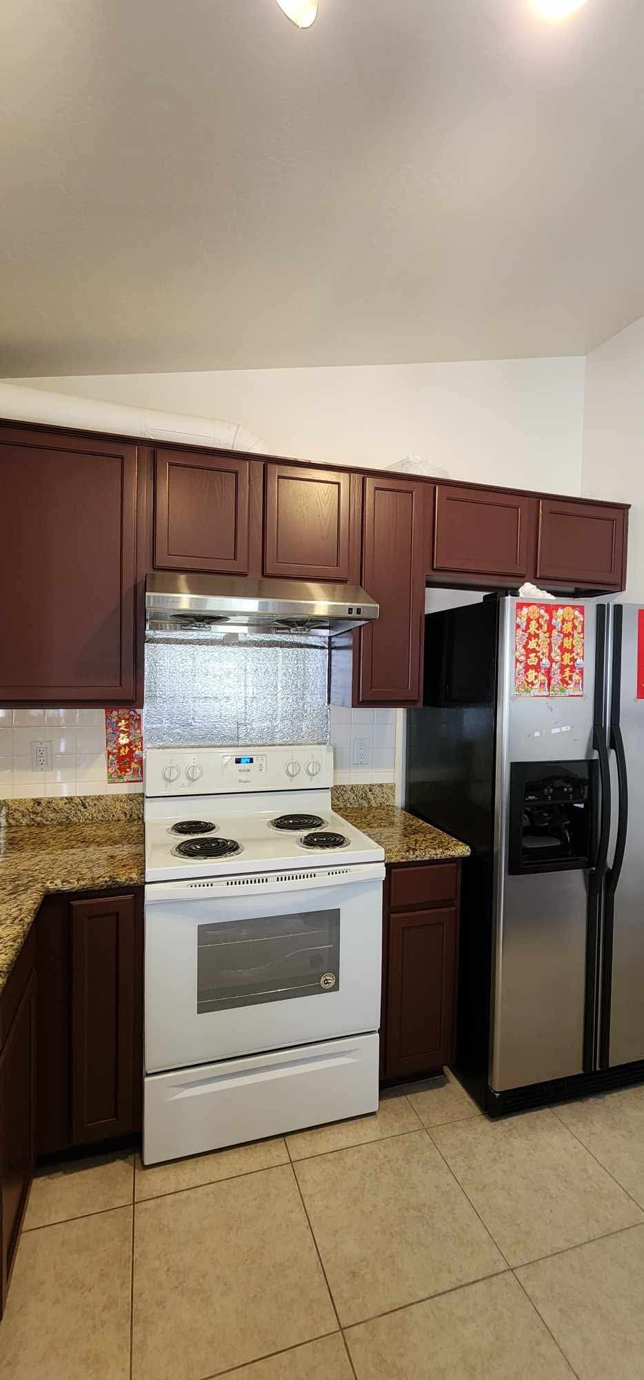 Small kitchen with brown cabinets, white stove, granite counters, and stainless steel refrigerator.