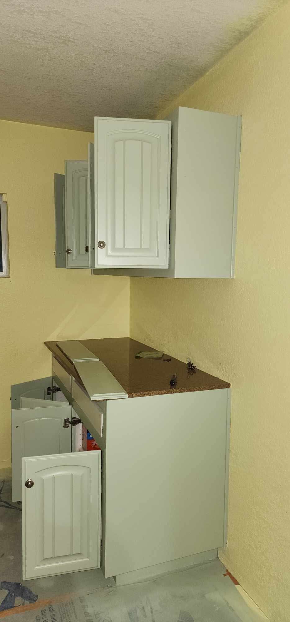 Small kitchen area with white cabinets, beige walls, and a sink under open wall cabinets.