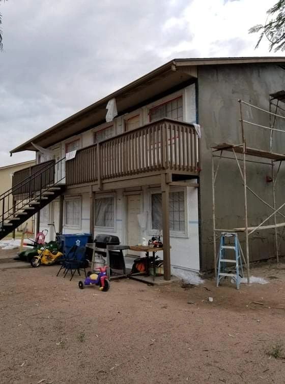 Rustic two-story house with balcony, exterior stairs, and scaffolding on a dirt lot