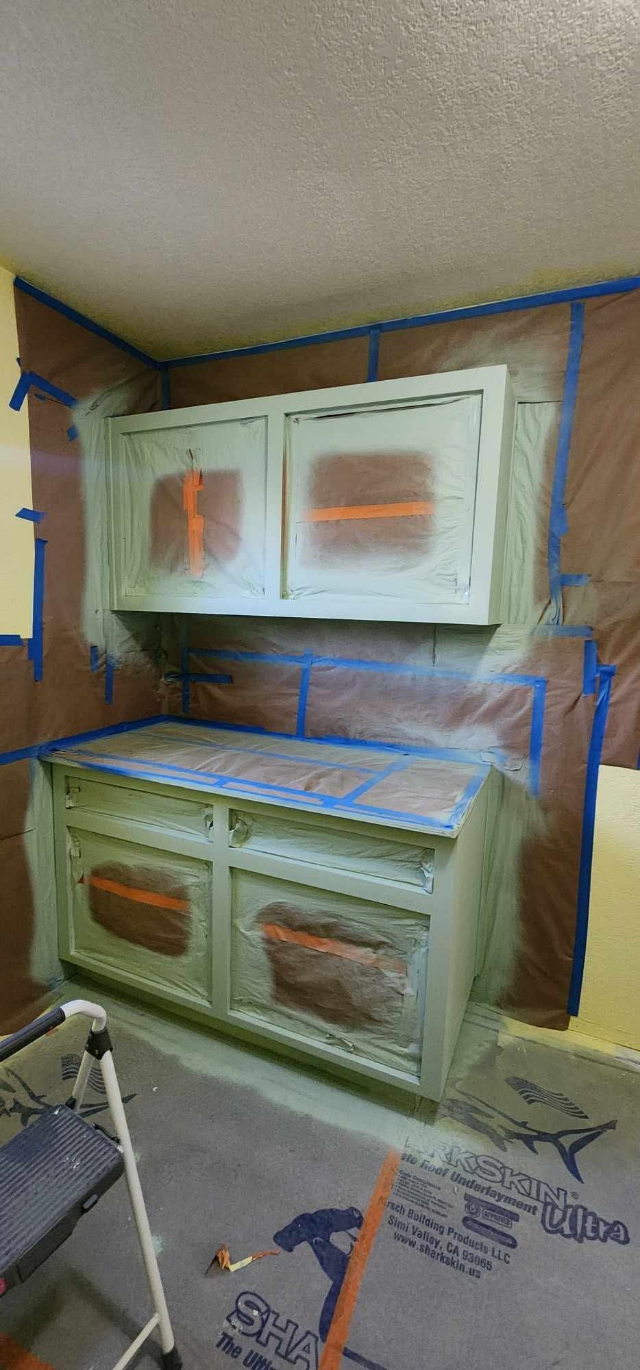 White kitchen cabinets and lower drawers under renovation, covered in plastic and masked for painting