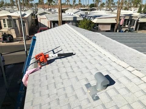 Worker repairing a white shingle roof with a safety rope on a sunny residential street