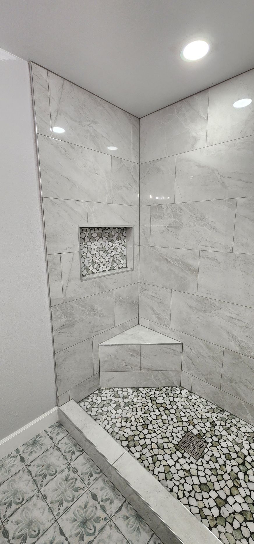 Corner shower with gray marble tile, pebble floor, and built-in niche and bench.