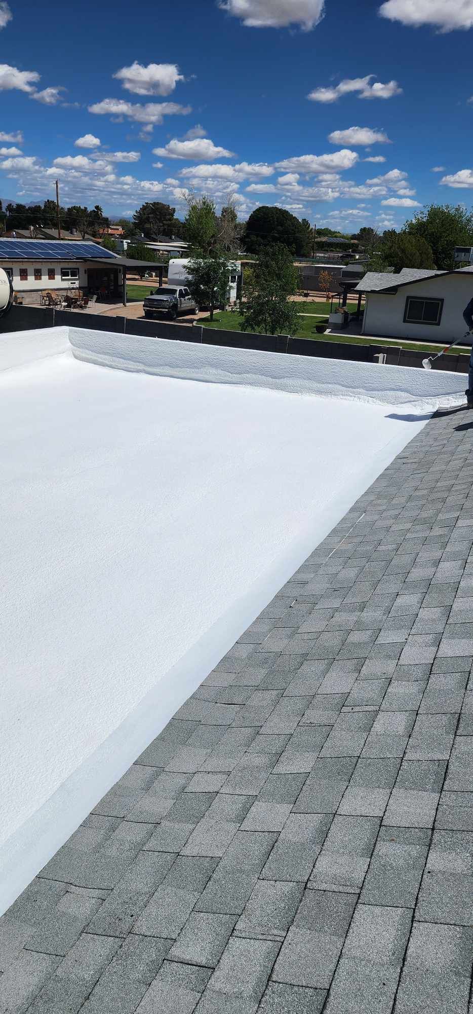 Rooftop with white snow or tarp beside gray shingles under a blue sky with clouds.