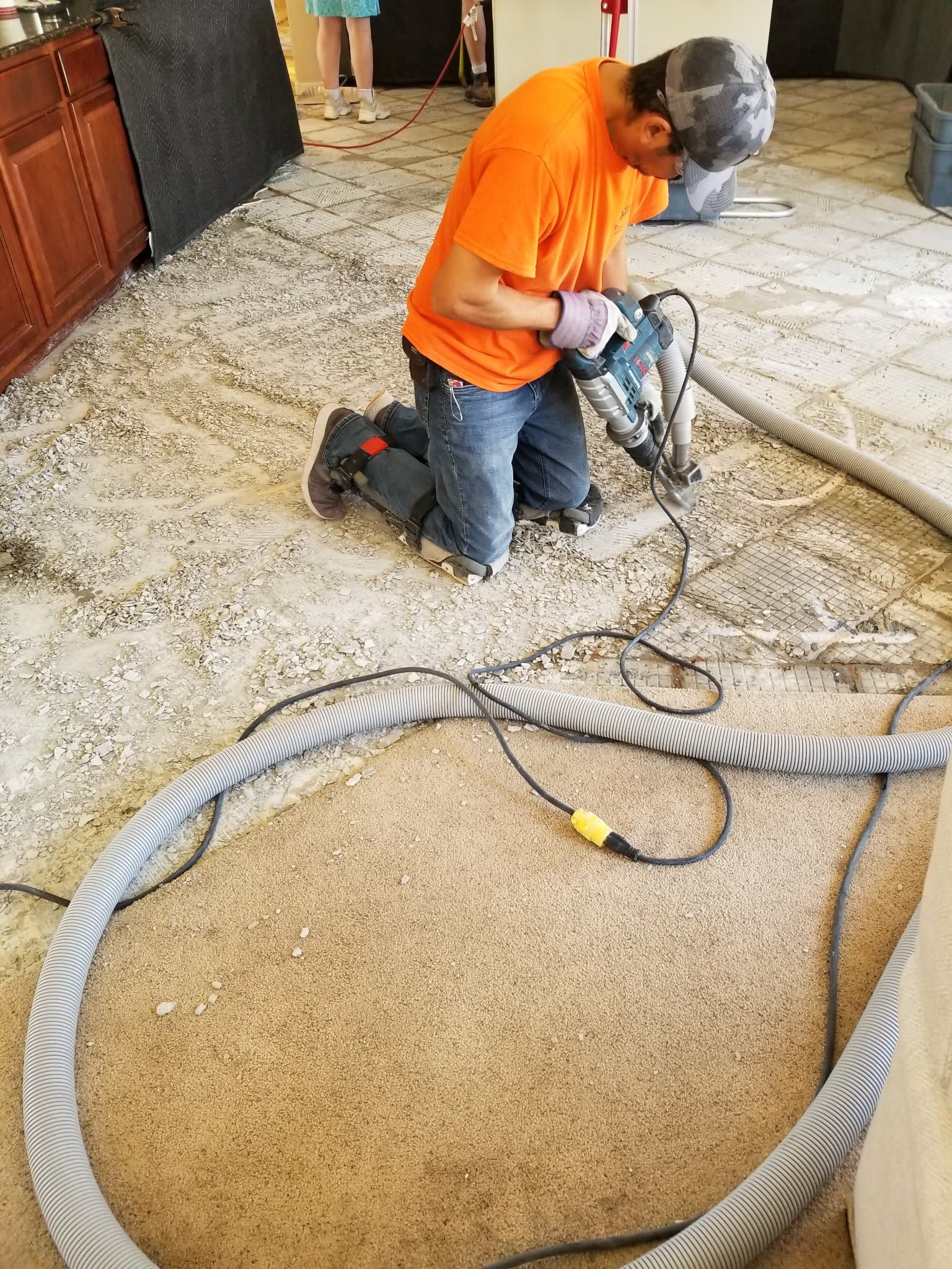 Worker using a floor buffer on a carpeted floor, with hoses and equipment in the foreground.