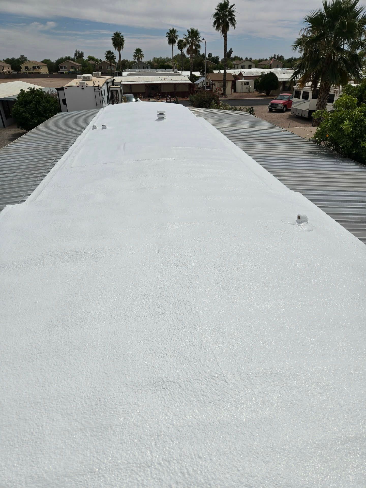 White rooftop under cloudy sky, with palm trees and desert homes in the background.