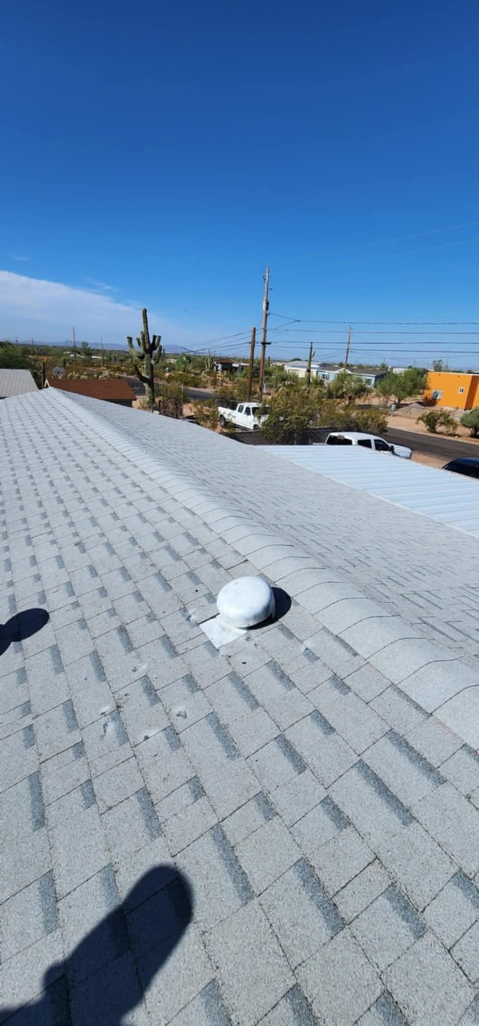 Rooftop with white shingles and vents, overlooking a sunny neighborhood under a clear blue sky