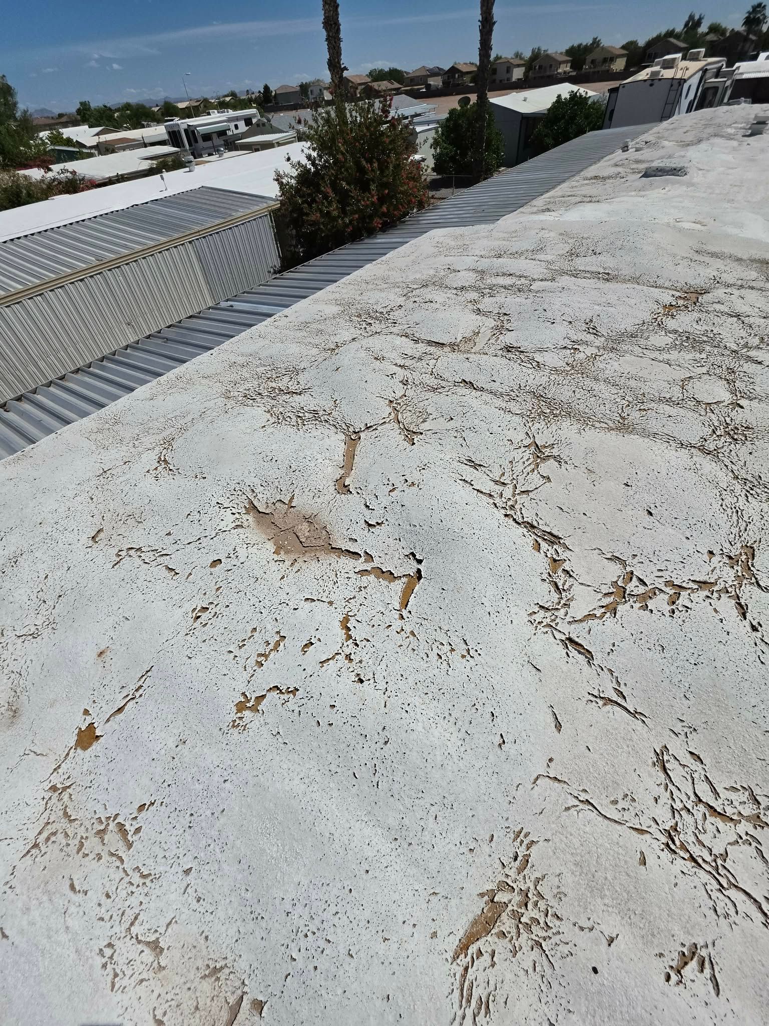 White, weathered rooftop with cracks and rust stains overlooking suburban houses and trees